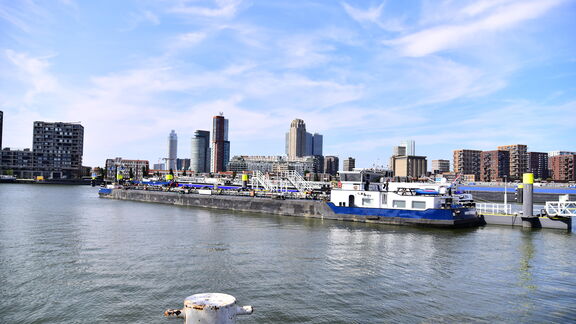 Uitzicht op de haven van Rotterdam met binnenschepen en de skyline op de achtergrond.