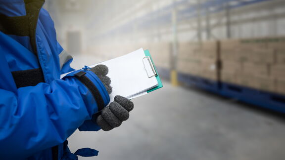 Persoon schrijft op notitieblok in een koelcel gevuld met containers