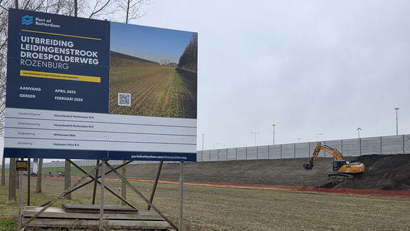 Bouwbord bij een projectlocatie met een graafmachine die op een talud aan het werk is.