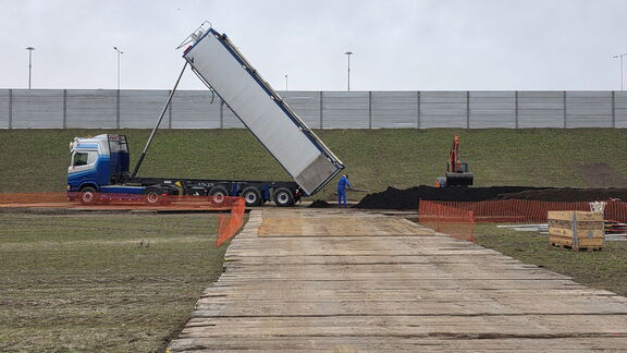 Vrachtwagen kiept aarde op een bouwterrein waar een graafmachine aan het werk is.