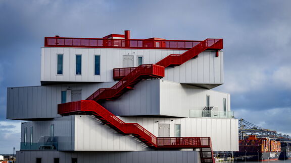 Modern wit gebouw met rode buitentrap in een havengebied.