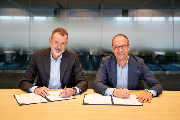 Twee personen die documenten ondertekenen aan een vergadertafel