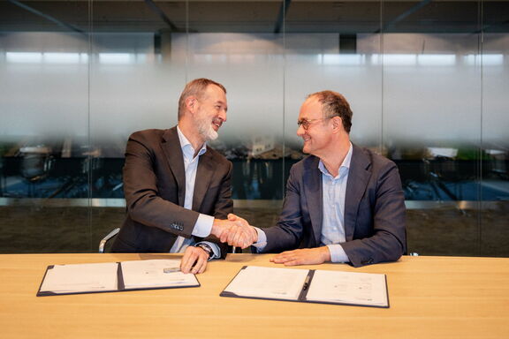 Two people shaking hands over signed documents in a meeting room