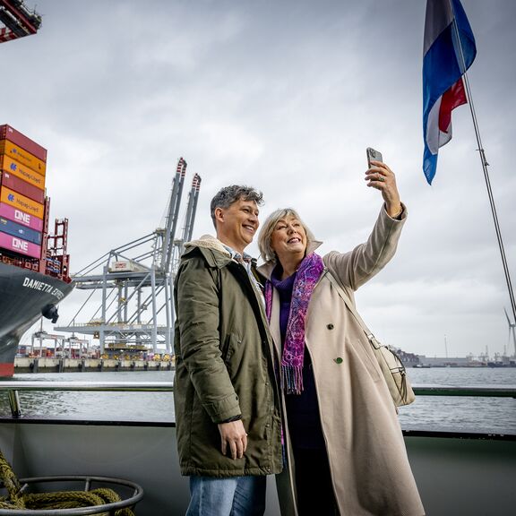 Mensen maken een selfie op de rondvaartboot van Portlantis met een groot containerschip op de achtergrond