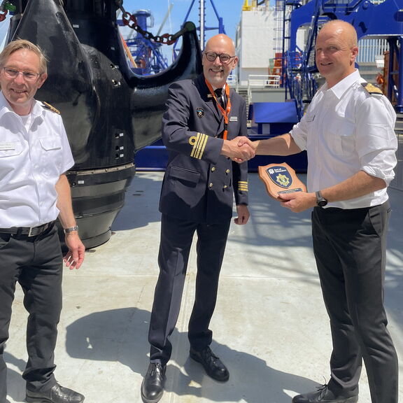 Ruud Hoogesteger, operationeel manager bij de Divisie Havenmeester, overhandigt het traditionele Rotterdamse havenschildje aan de bemanning van het schip.