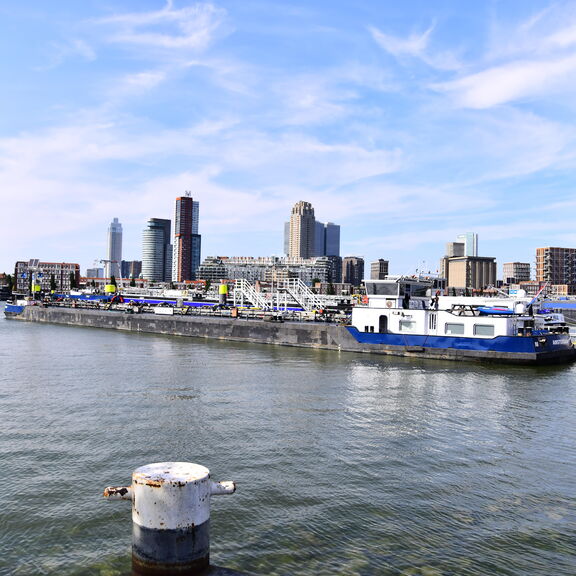 Uitzicht op de haven van Rotterdam met binnenschepen en moderne gebouwen op de achtergrond.