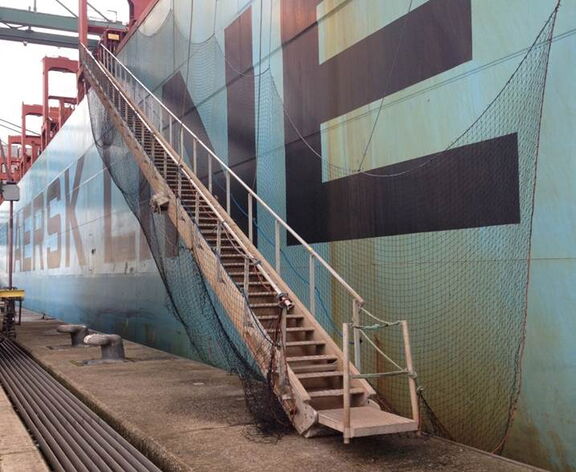 Een loopbrug met trap die vanaf de kade naar een groot vrachtschip leidt, met veiligheidsnetten langs de zijkant van het schip