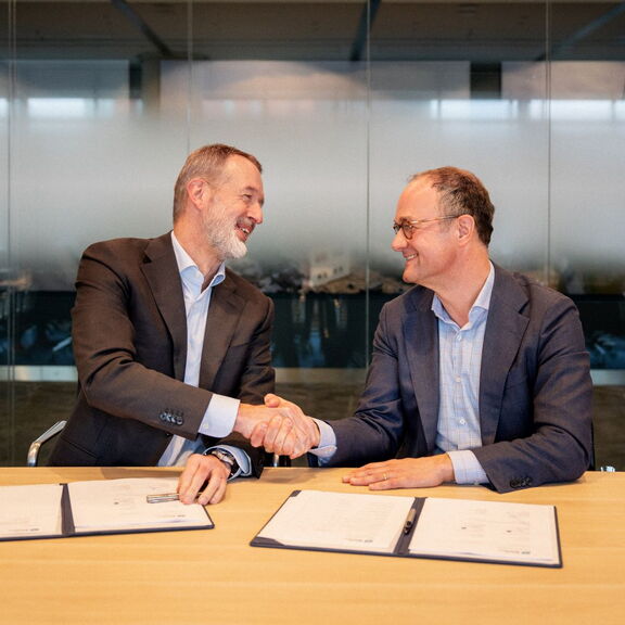 Twee personen die elkaar de hand schudden boven ondertekende documenten in een vergaderruimte