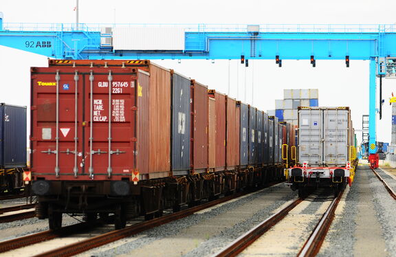 Goederentreinen met containers op meerdere sporen onder een blauwe kraan."